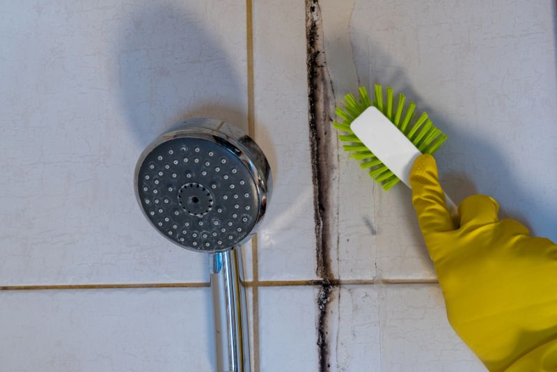 scrubbing mould on the bathroom wall near the shower head with a brush