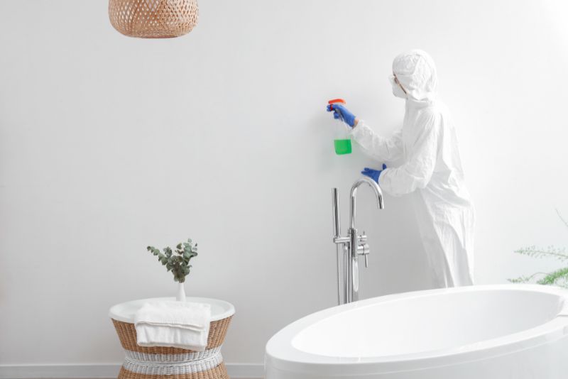 worker in protective gear cleaning mould on a white wall